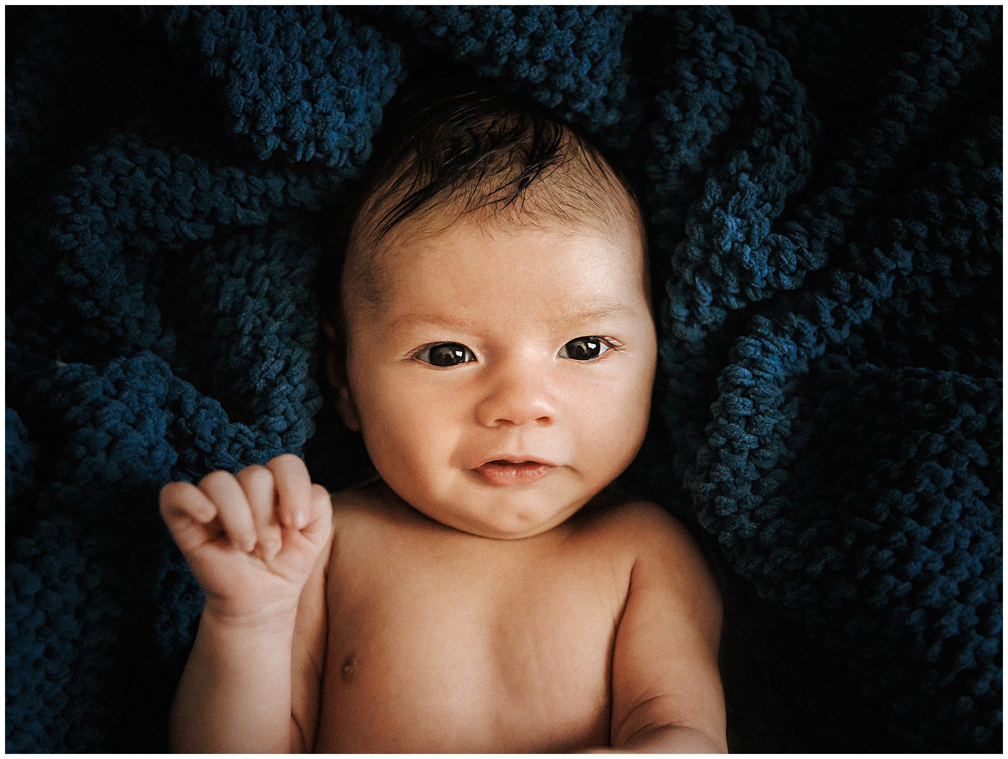Portrait of newborn baby boy smiling, laying in dark blue knit blanket