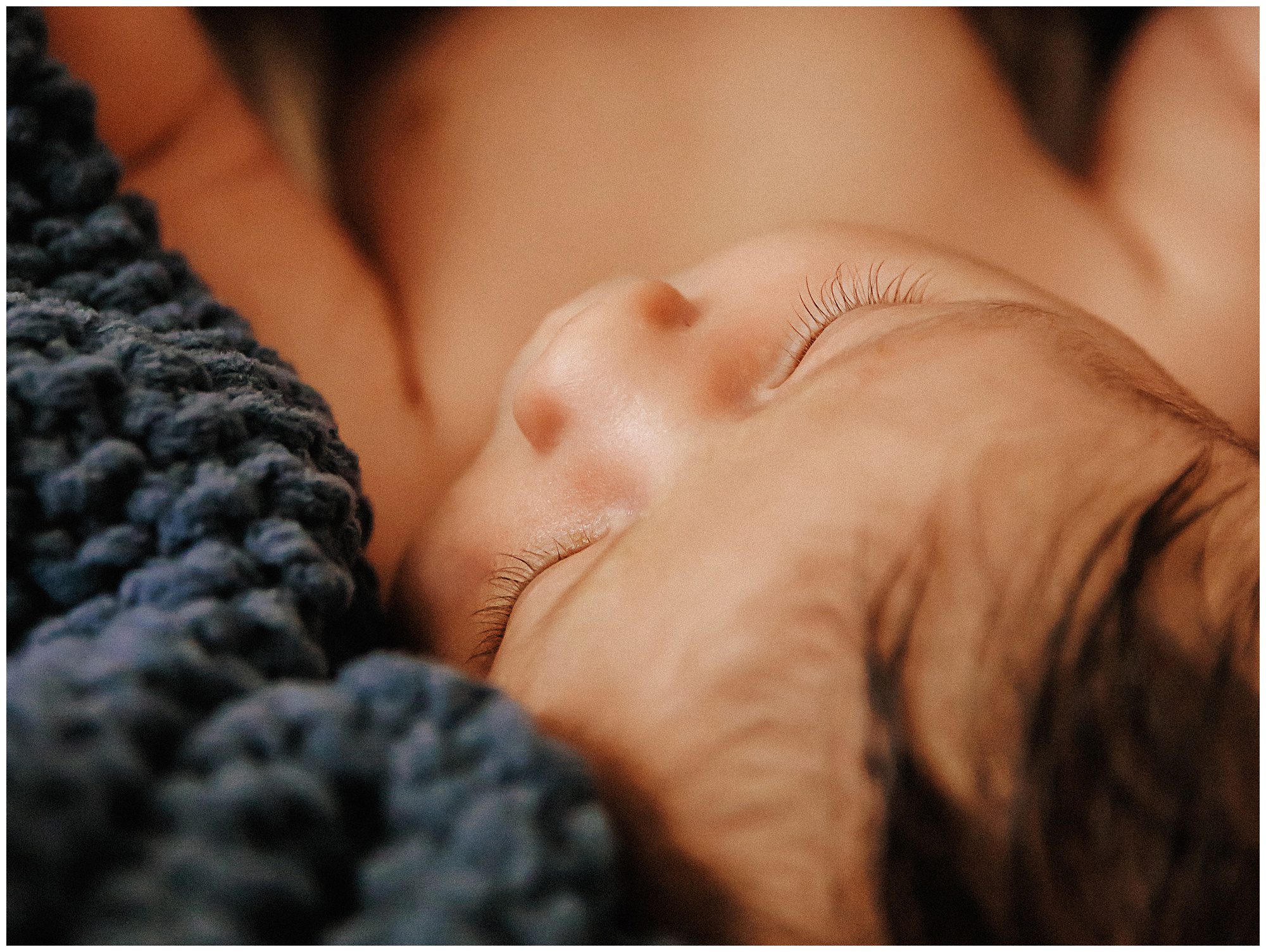 Portrait of newborn baby boy smiling, laying in dark blue knit blanket