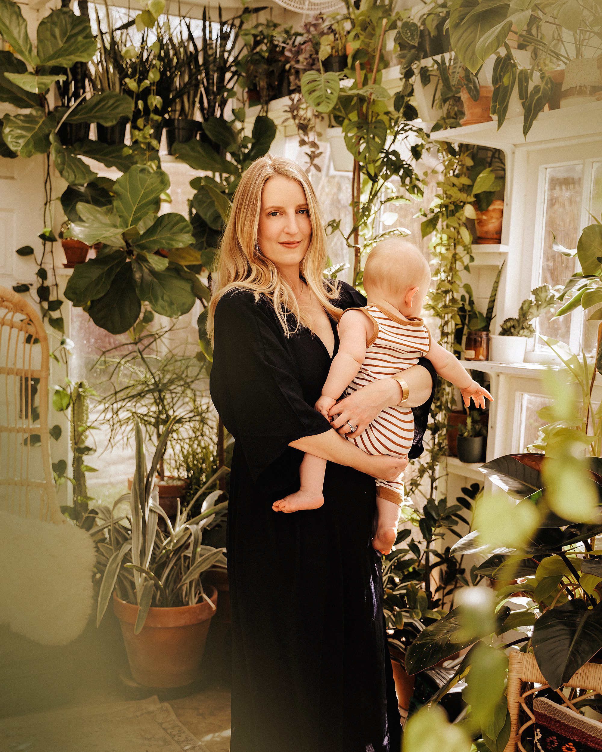 Mom looks at camera while holding her infant son in a greenhouse in Nashville