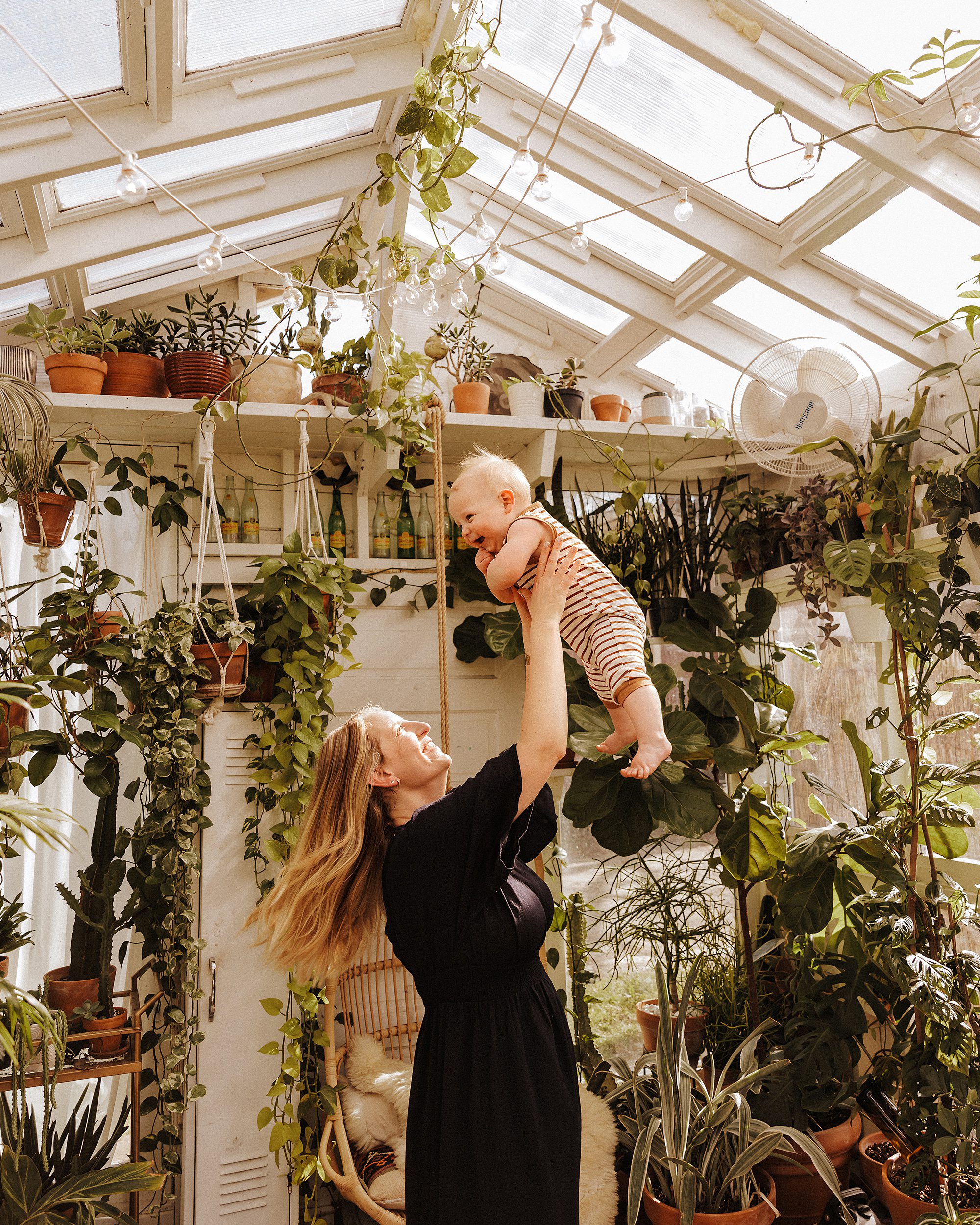 Mom tosses baby boy up in the air during mini session in East Nash Greenhouse