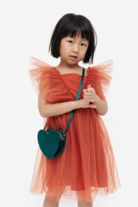 Product Photo of little girl wearing a burnt orange tulle dress and wearing a heart shaped purse