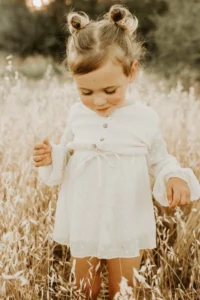 Product photo of a little girl wearing a polka dot print cream dress with button details