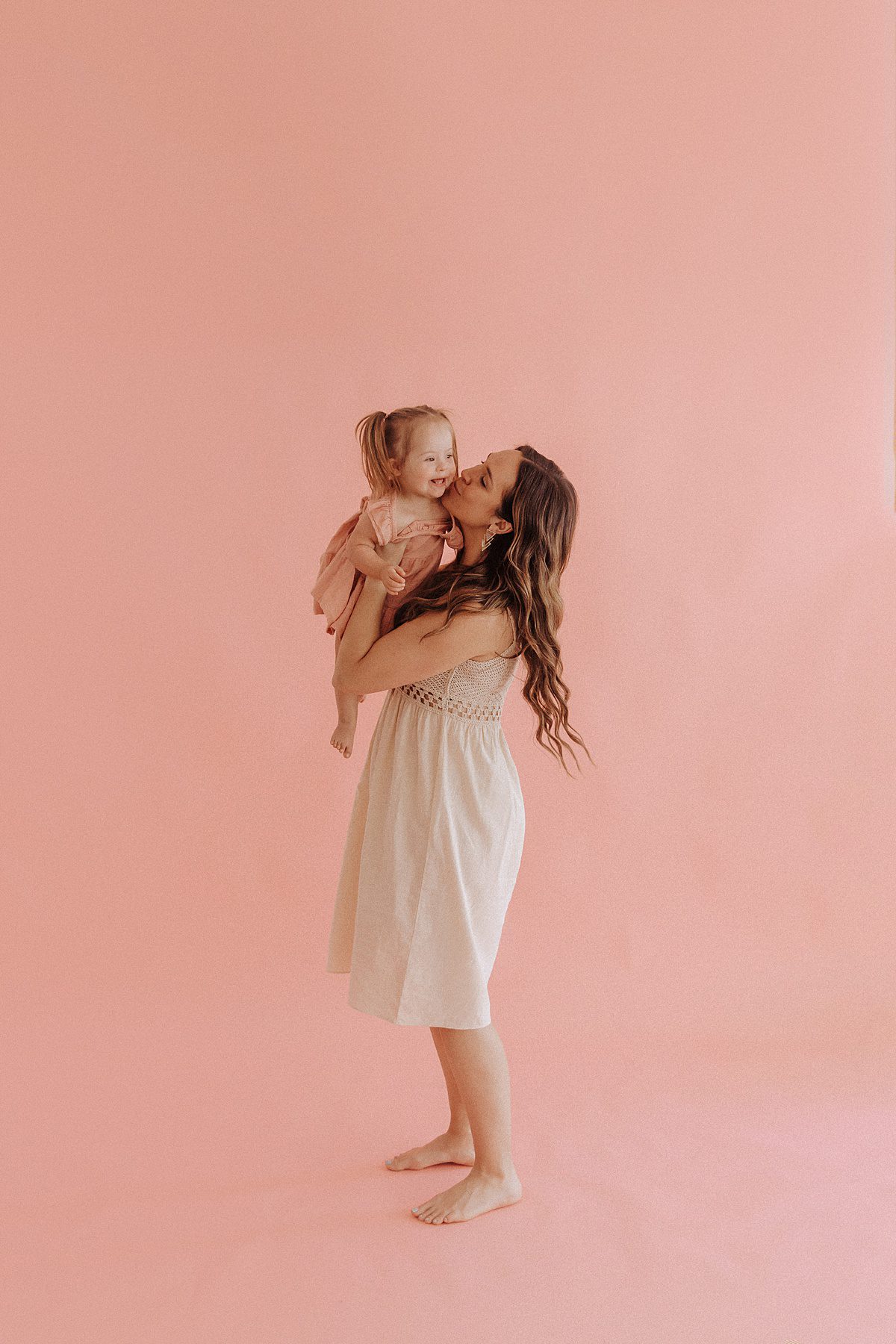 Mother holds her toddler up and gives her a kiss during a photoshoot