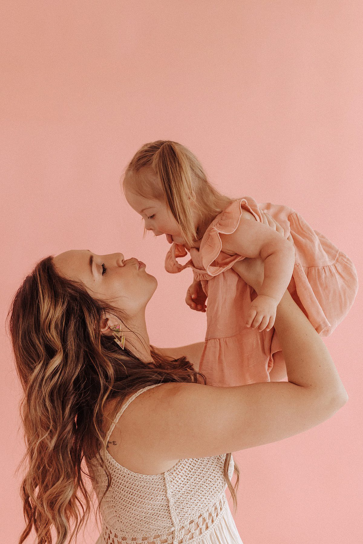 Mother holds her toddler up to give her a kiss during a studio mini session for Mother's Day