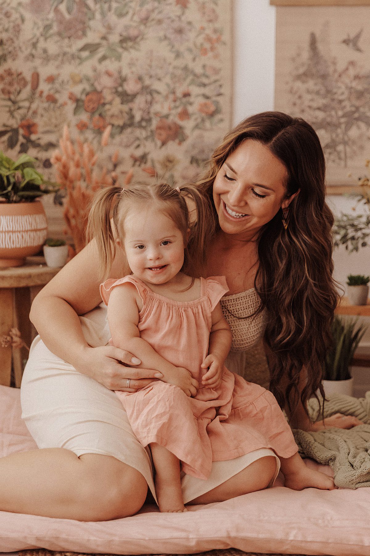 Little girl sits on her mother's lap and smiles at the camera for a photoshoot