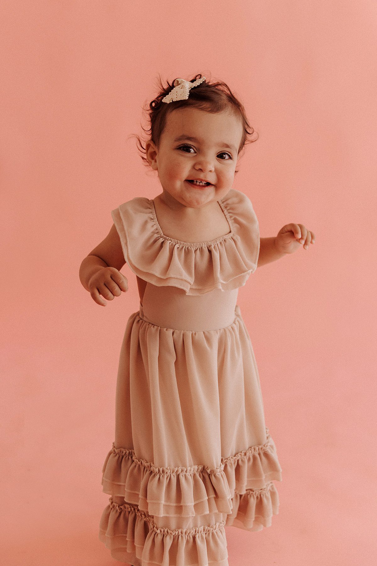 Little girl with dark brown hair and tan dress smiles